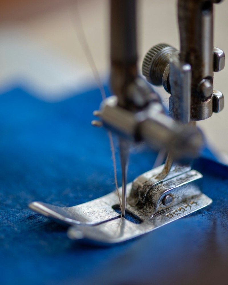 Close-up of a sewing machine needle and presser foot stitching a seam in blue fabric.