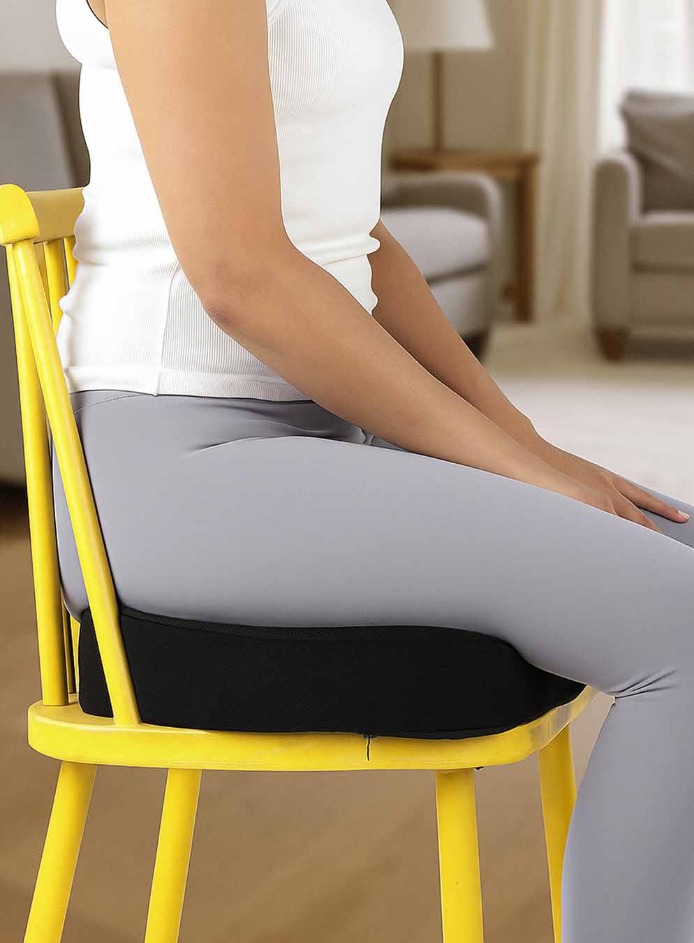 Black memory foam coccyx cushion positioned on a yellow chair seat.