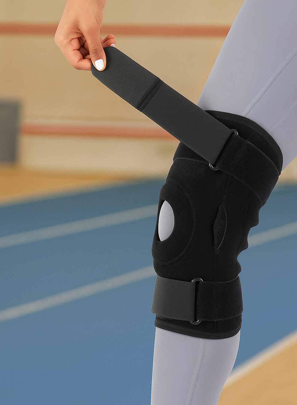 Model adjusting the black hinged knee brace with an open patella cutout on the knee.