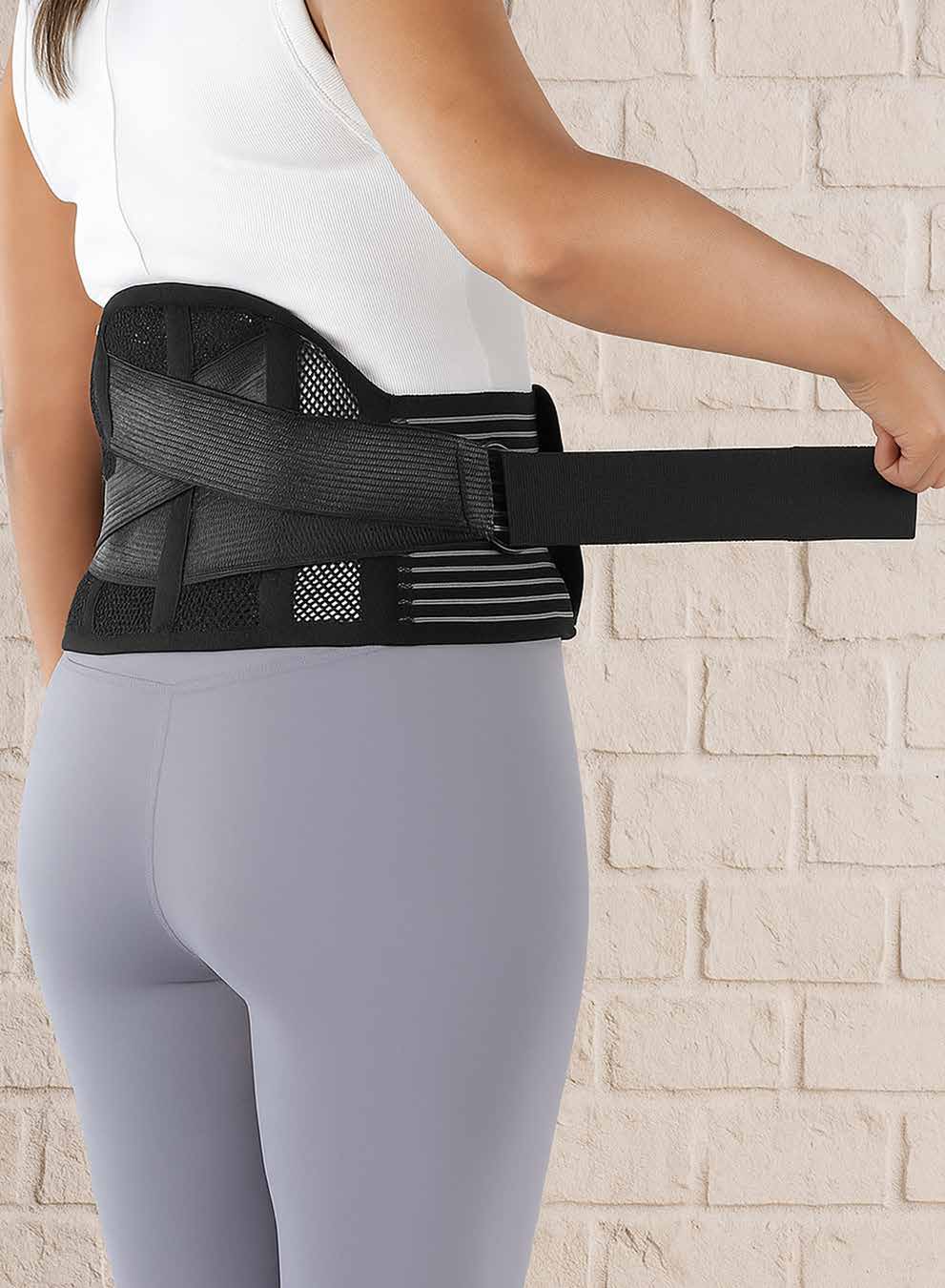 Model fastening the black mesh lumbar sacral belt around the lower back and waist.
